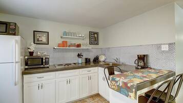 Cocina compacta con armarios blancos, microondas, cafetera y salpicadero de azulejos.