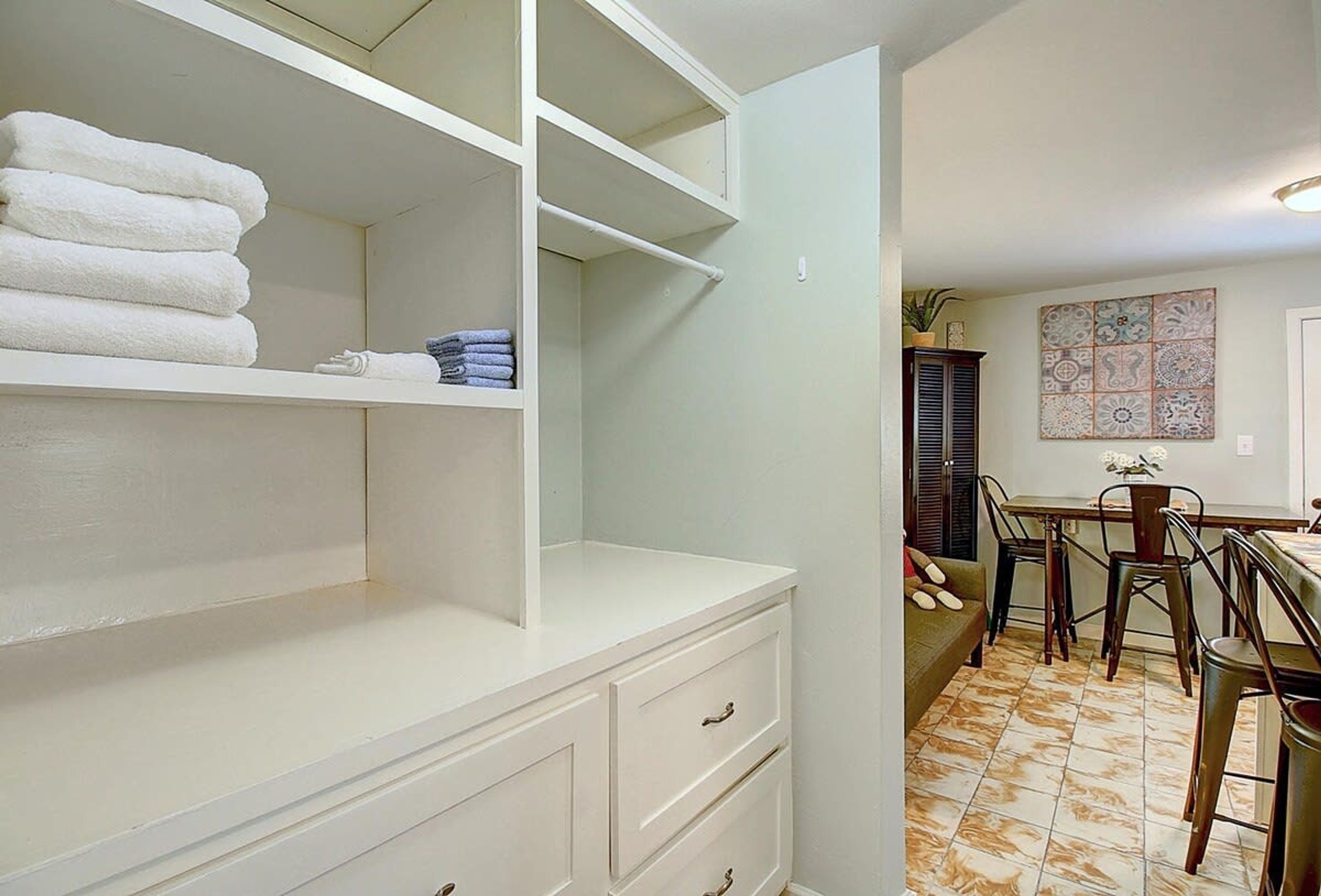 Casa de banho branca com prateleira embutida para toalhas, toucador branco com gavetas e chão em azulejo.