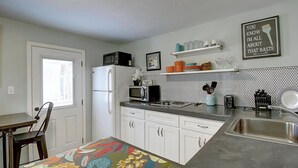 A kitchen with white cabinets, a refrigerator, a microwave, a sink, and a countertop with various items. - Kona Cottage Dog Friendly In Town Location (Port Aransas)