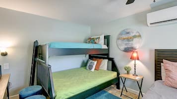 Uma cama de beliche com colchão verde, uma mesinha de cabeceira com abajur e um quadro redondo na parede.