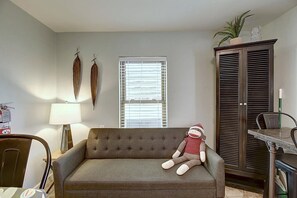 Ein Wohnzimmer mit einer Couch, einer Lampe, einem Fenster mit Jalousien, einem Schrank und einem kleinen Tisch.