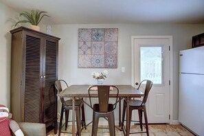 A dining area with a table, chairs, a cabinet, and a decorative tile wall. - Kona Cottage Dog Friendly In Town Location (Port Aransas)