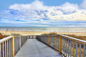 A wooden boardwalk leading to a beach with a clear view of the ocean and a partly cloudy sky. - Incredible Ocean Views Direct Beach Access Pool (Port Aransas)