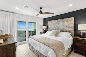 A bedroom with a bed, a ceiling fan, a view through a window, and a nightstand with a lamp. - Incredible Ocean Views Direct Beach Access Pool (Port Aransas)