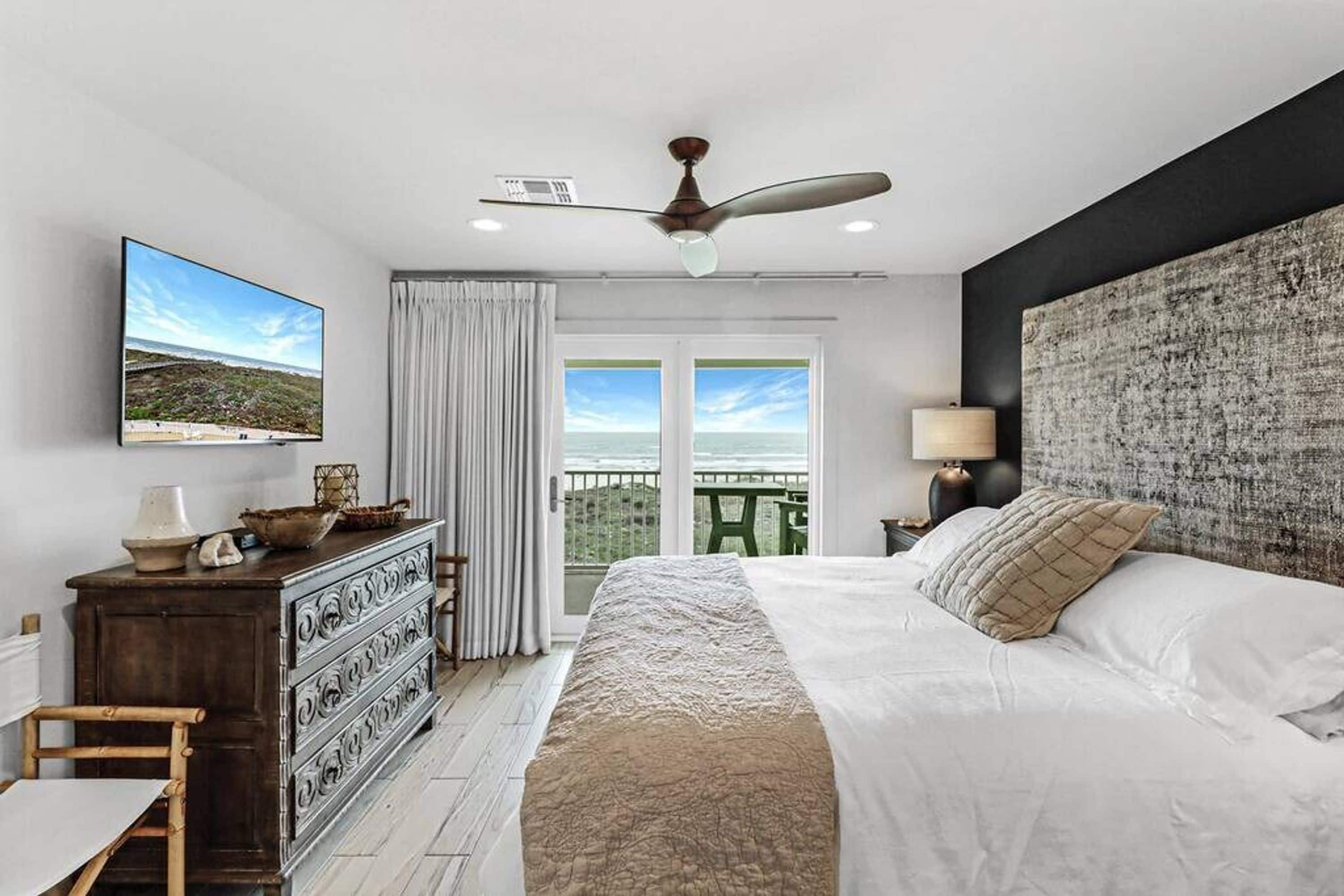 A bedroom with a bed, dresser, television, and a view of the outdoors.
