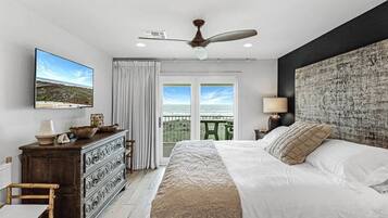 A bedroom with a bed, dresser, television, and a view of the outdoors.
