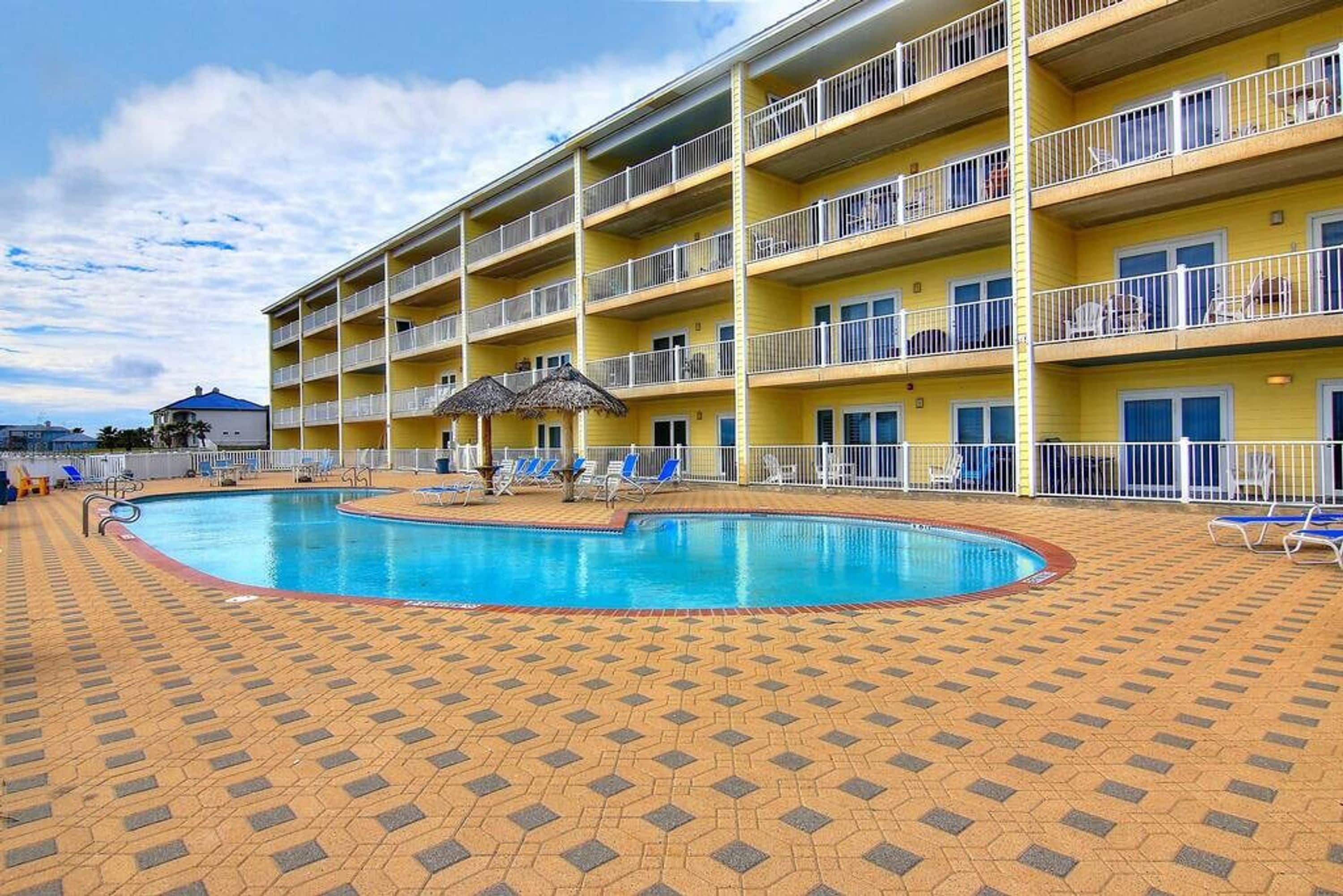 A multi-story hotel with a swimming pool surrounded by lounge chairs and umbrellas.