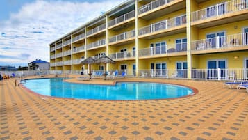 A multi-story hotel with a swimming pool surrounded by lounge chairs and umbrellas.