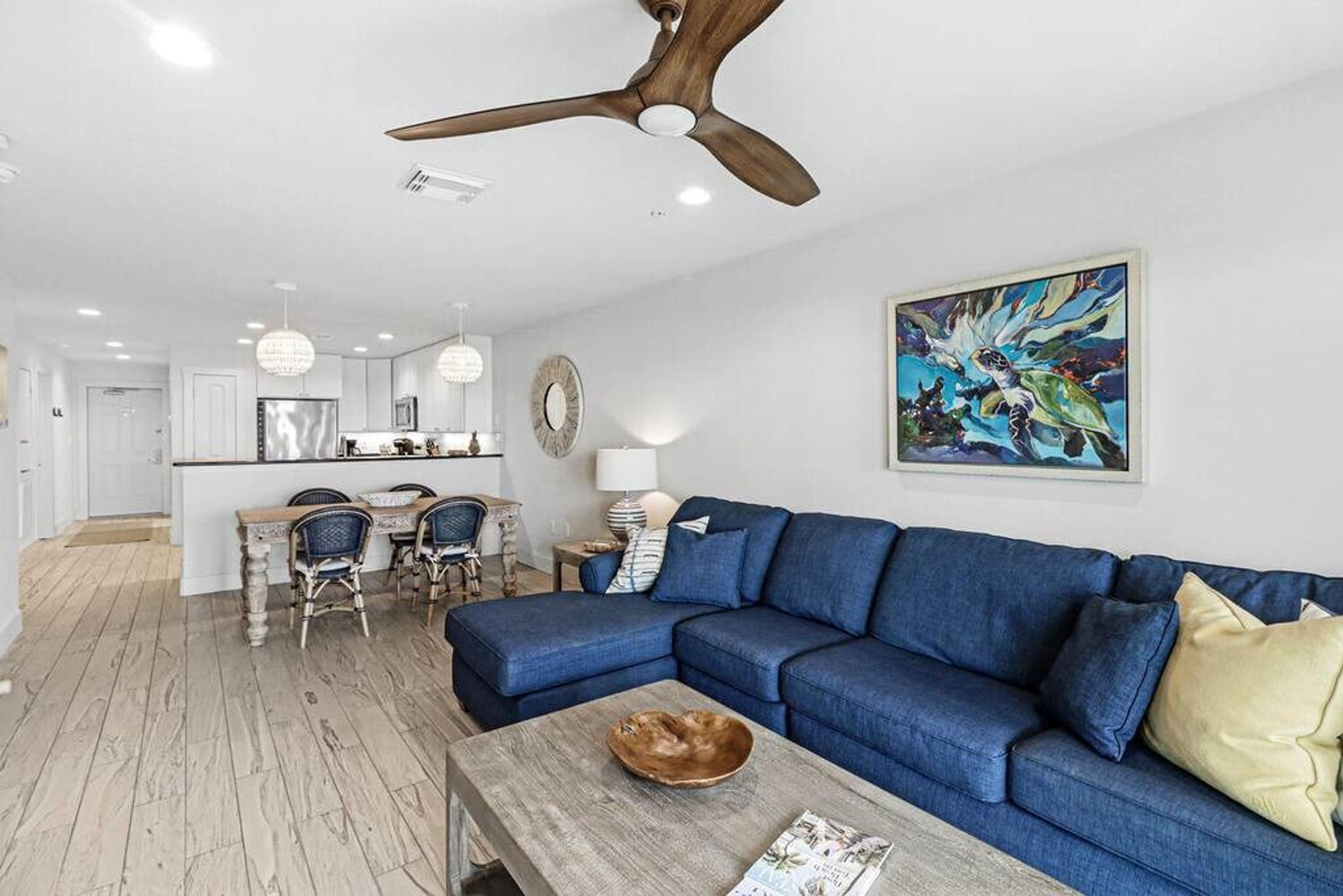 A modern living room with a blue sofa, a wooden coffee table, and a ceiling fan.