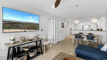A modern living room with a large flat-screen TV, a sofa, and a dining area with chairs and a table.