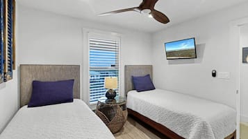 A bedroom with two beds, a ceiling fan, a window with blinds, a bedside lamp, and a wall-mounted picture.