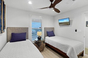 A bedroom with two beds, a ceiling fan, a window with blinds, a bedside lamp, and a wall-mounted picture. - Incredible Ocean Views Direct Beach Access Pool (Port Aransas)