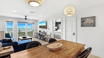 A spacious living area with a wooden dining table, a blue sofa, and a balcony with a view.