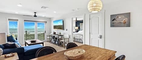 A spacious living area with a wooden dining table, a blue sofa, and a balcony with a view.