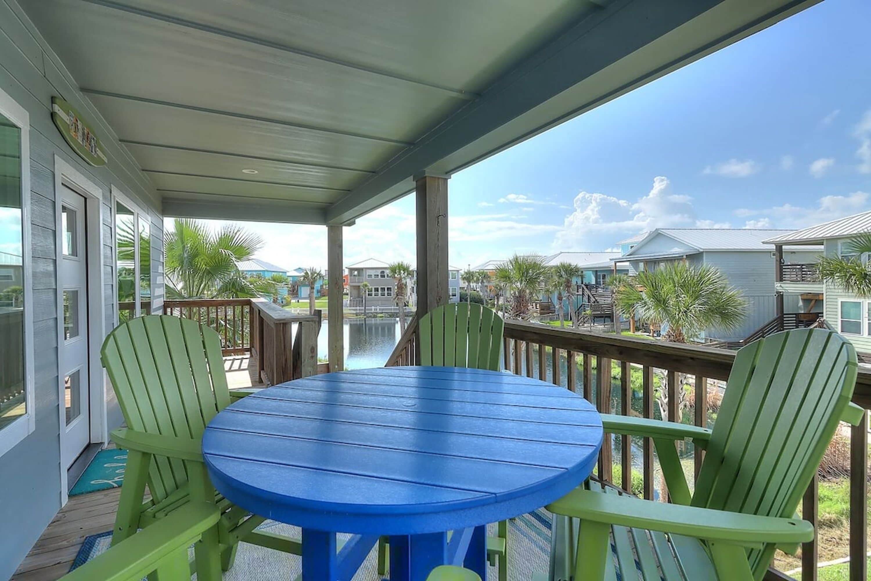 A covered outdoor area with a blue table and green chairs, overlooking a residential neighborhood.