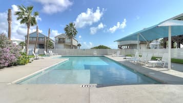 A swimming pool with lounge chairs, palm trees, and a clear sky.