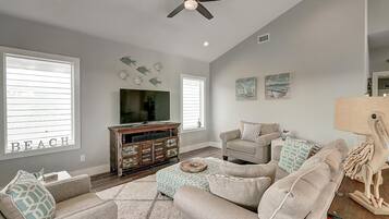 A living room with a ceiling fan, a television, a sofa, and decorative wall art.