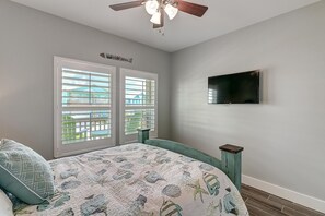 A bedroom with a bed, a ceiling fan, a TV mounted on the wall, and a window with blinds. - Paradise Vibes- Pond Views 2 Balconies (Port Aransas)