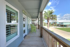 A covered porch with a view of palm trees and a building in the background. - Paradise Vibes- Pond Views 2 Balconies (Port Aransas)