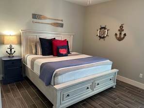 A bedroom with a bed, nightstands, a lamp, and nautical-themed wall decor. - Paradise Vibes- Pond Views 2 Balconies (Port Aransas)