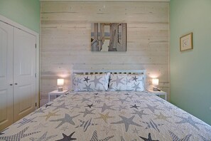 Une chambre à coucher avec un lit, deux tables de chevet, une commode, une porte et un tableau encadré au mur.