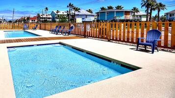 A swimming pool with a wooden deck and lounge chairs.