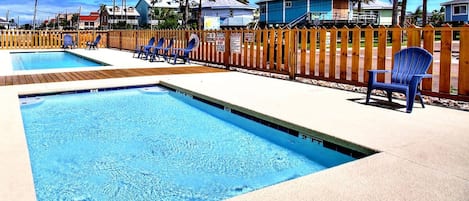 Una piscina con terraza de madera y sillones de descanso.