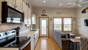 A compact kitchen with a microwave, stove, and sink, leading to a living area with a sofa and a TV. - Sweet Home La Cabana Patio BBQ Community Pool (Port Aransas)