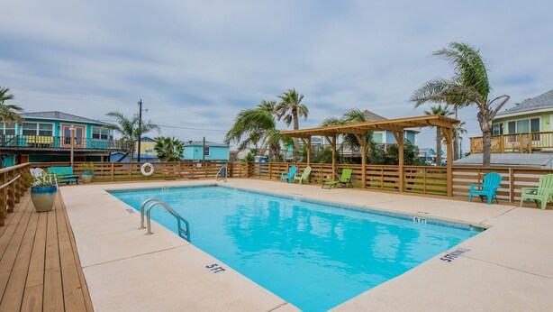 Ein Schwimmbecken mit Holzterrasse, Liegestühlen und einem überdachten Bereich mit einer Pergola.