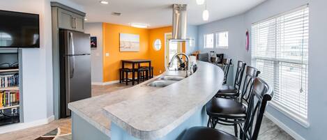 A modern kitchen with a central island, bar stools, a built-in refrigerator, and a dining area with a table and chairs.