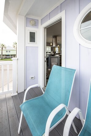 A porch with two white chairs and a teal cushion, a door leading to a kitchen, and a small window with a round light fixture. - Maui East- Pet Friendly 3 Blocks to Beach (Port Aransas)