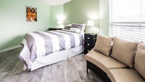 Ein Schlafzimmer mit einem Bett, Nachttischen, einer Lampe, einem Sofa und einem Gemälde an der Wand.