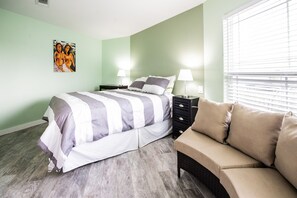 Ein Schlafzimmer mit einem Bett, Nachttischen, einer Lampe, einem Sofa und einem Gemälde an der Wand.