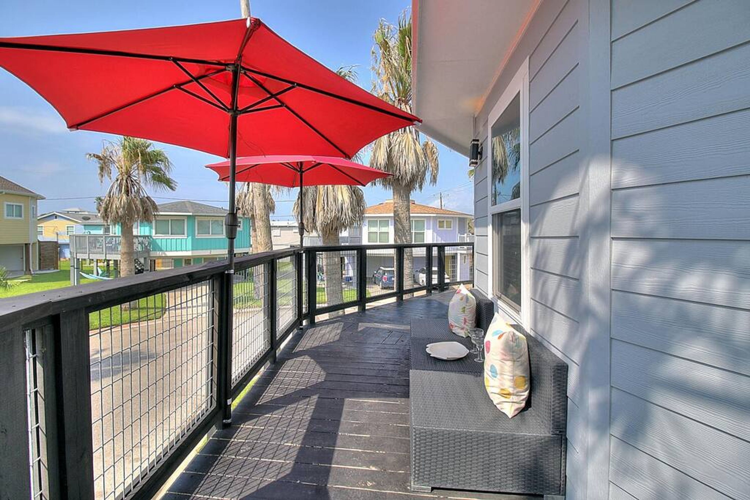 Un espace extérieur abrité, doté d’une rambarde en métal, d’une table avec un coussin et de parasols rouges.