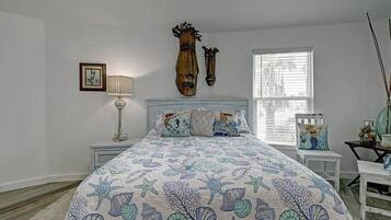 Une chambre à coucher avec un lit, une table de chevet, une lampe, un tableau encadré et une fenêtre avec des stores.