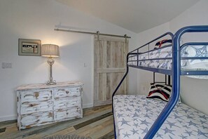 A bunk bed with a patterned mattress, a dresser with a distressed finish, a lamp, and a door with a wooden panel. - La Sirena Pet Friendly Community Pool (Port Aransas)
