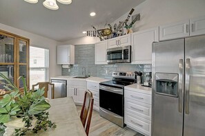 A modern kitchen with stainless steel appliances, white cabinetry, and a dining area with a wooden table and chairs. - La Sirena Pet Friendly Community Pool (Port Aransas)