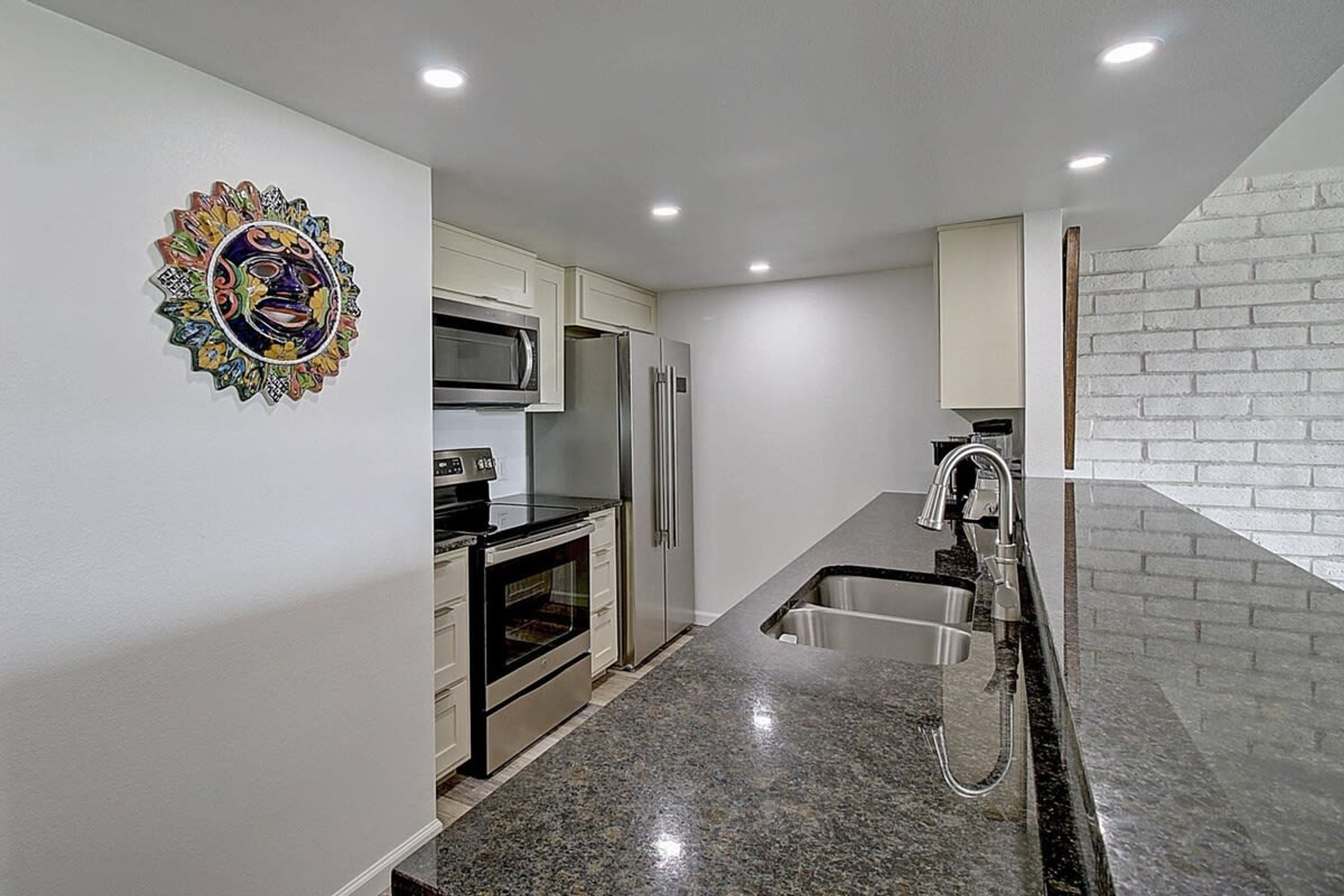 A modern kitchen with stainless steel appliances, a granite countertop, and a decorative wall piece.
