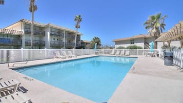 Ein Swimmingpool mit Liegestühlen und einem eingezäunten Bereich, umgeben von mehrstöckigen Gebäuden mit Balkonen.
