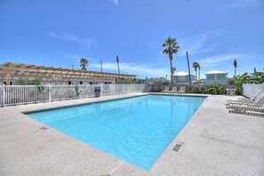 Una piscina rectangular con una cerca blanca y sillones de descanso a un lado.