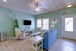 A room with a ceiling fan, a television, a blue sofa, a wooden table, and a green chair. - Blue Wave Community Pool Family Friendly Sleeps 10 (Port Aransas)