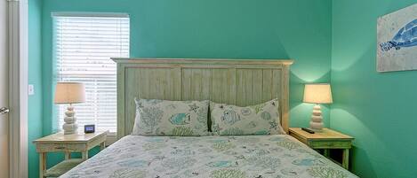 A bedroom with a bed, two bedside tables, a window with blinds, and a wall painting.