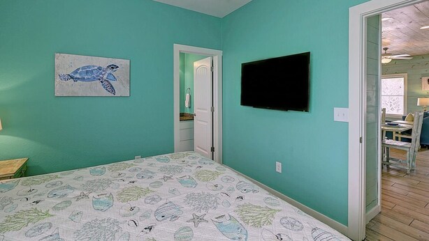 Een slaapkamer met turquoise wanden, een bed met een marine gestreept dekbedovertrek, een flatscreen televisie en een deur die naar een andere kamer leidt.