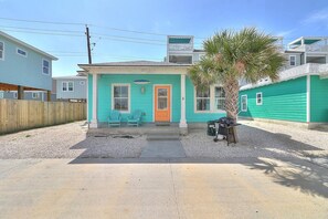 Een gelijkvloers huis met een veranda, een klein terras en een palmboom.