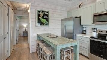 A kitchen with a wooden table, stools, a refrigerator, a microwave, and a stove.