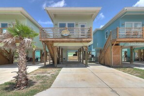 Un hotel frente a la playa con un paseo central, balcones de madera y una palmera.