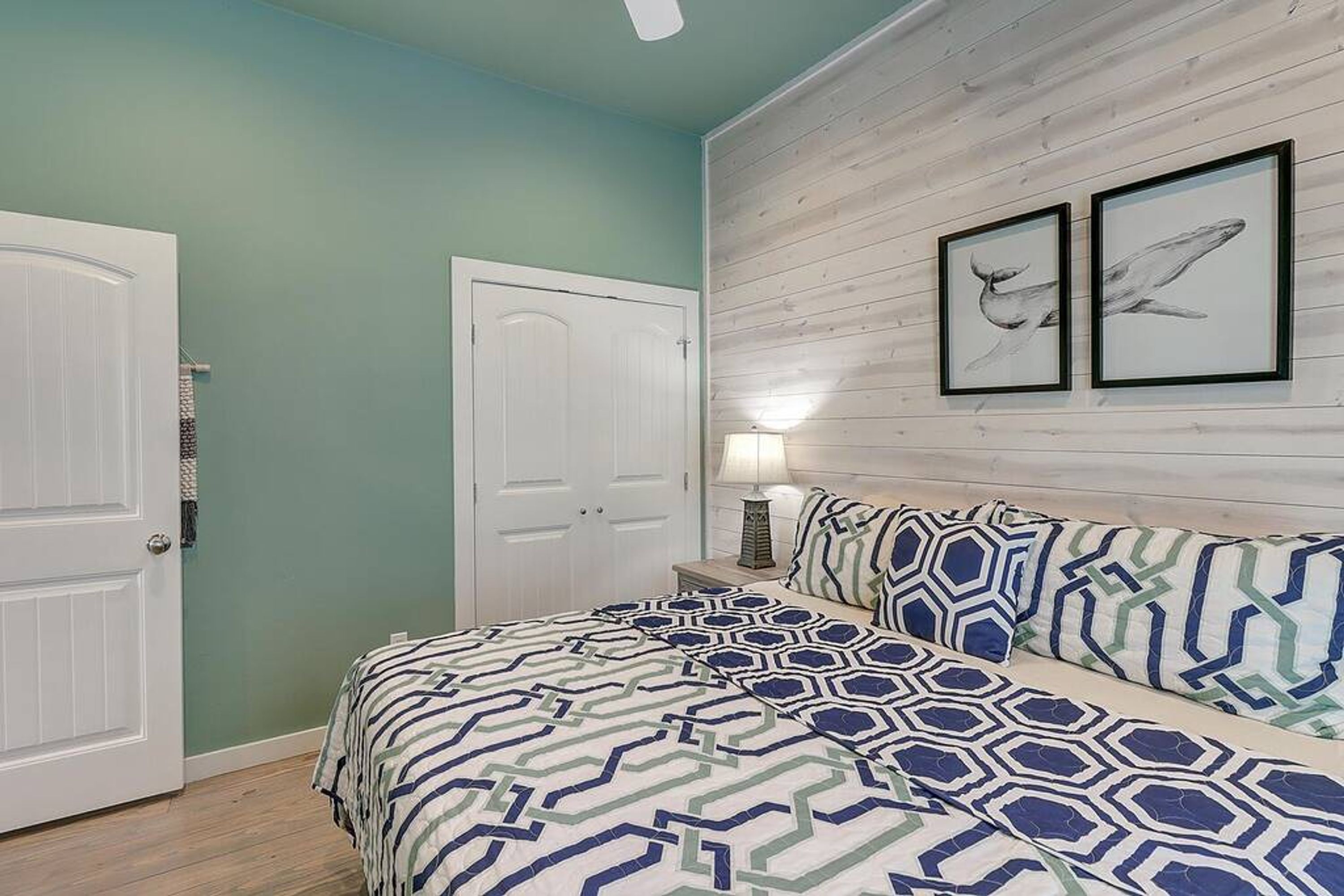 Une chambre à coucher avec un lit, deux tableaux encadrés au mur, une table de chevet et une porte.