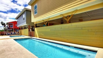 Una piscina con cubierta de madera, junto a un edificio de color amarillo y otro edificio rojo al fondo.