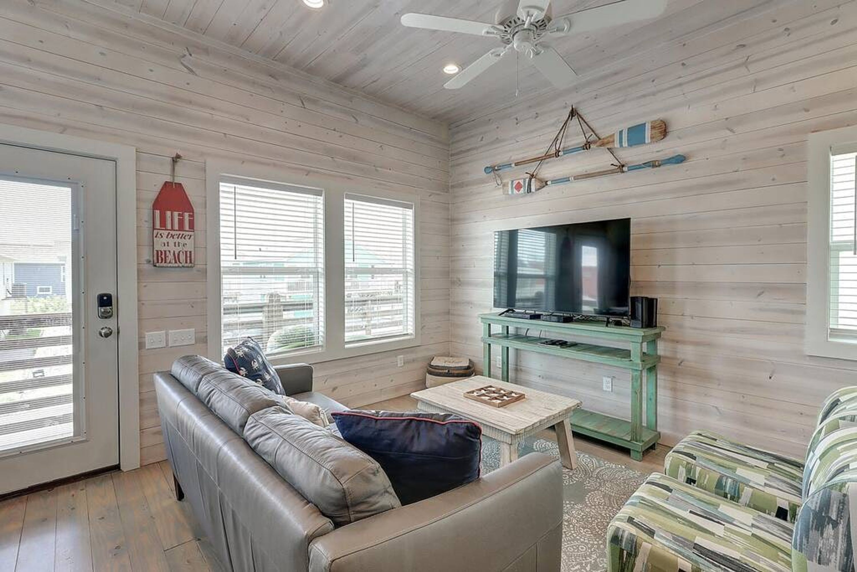Un salon avec un canapé en cuir, un téléviseur posé sur un meuble vert et un ventilateur de plafond.