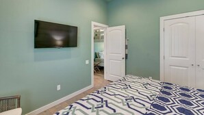 Una camera da letto con un letto, una televisione montata a parete e una porta che dà su un bagno.
